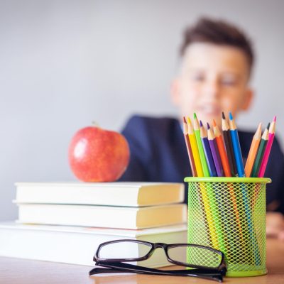 Schoolboy smiling behind a desk with books, pencils, and an alarm clock symbolizing study and creativity.